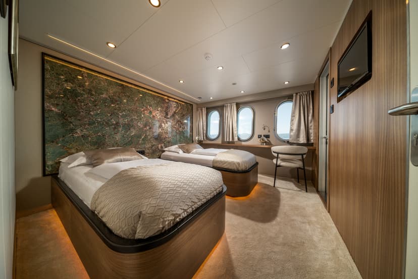 Twin cabin interior on a vessel with oval windows showing the sea and a green marble accent wall.