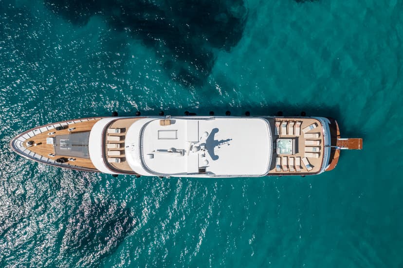 Aerial view of a white luxury yacht anchored in bright turquoise, sparkling sea water.