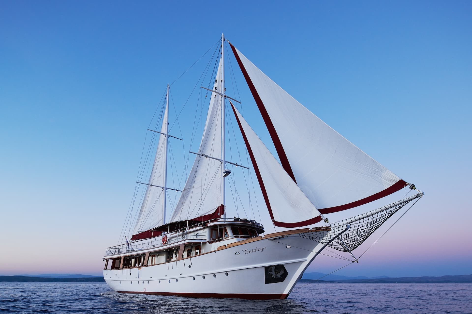 The yacht Cataleya sailing on blue water with distant mountains at sunset