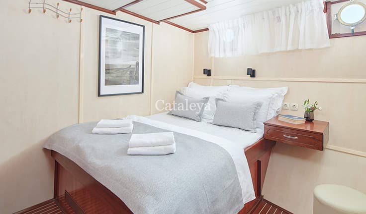Cabin interior with double bed, white linens, and wood trim, likely on a boat.