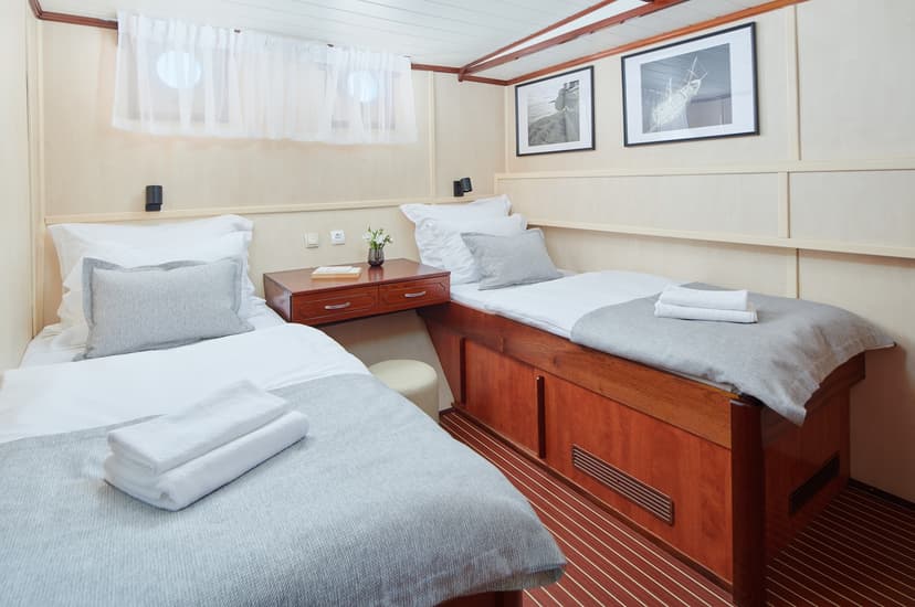 Twin cabin interior with wood paneling, white bedding, and framed artwork on a boat.