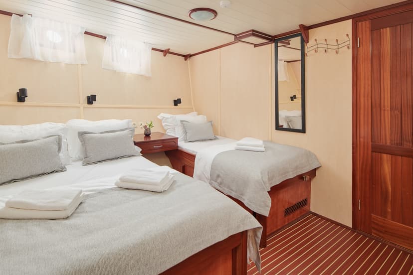 Triple cabin interior with two beds, wood paneling, and striped flooring, likely on a boat.