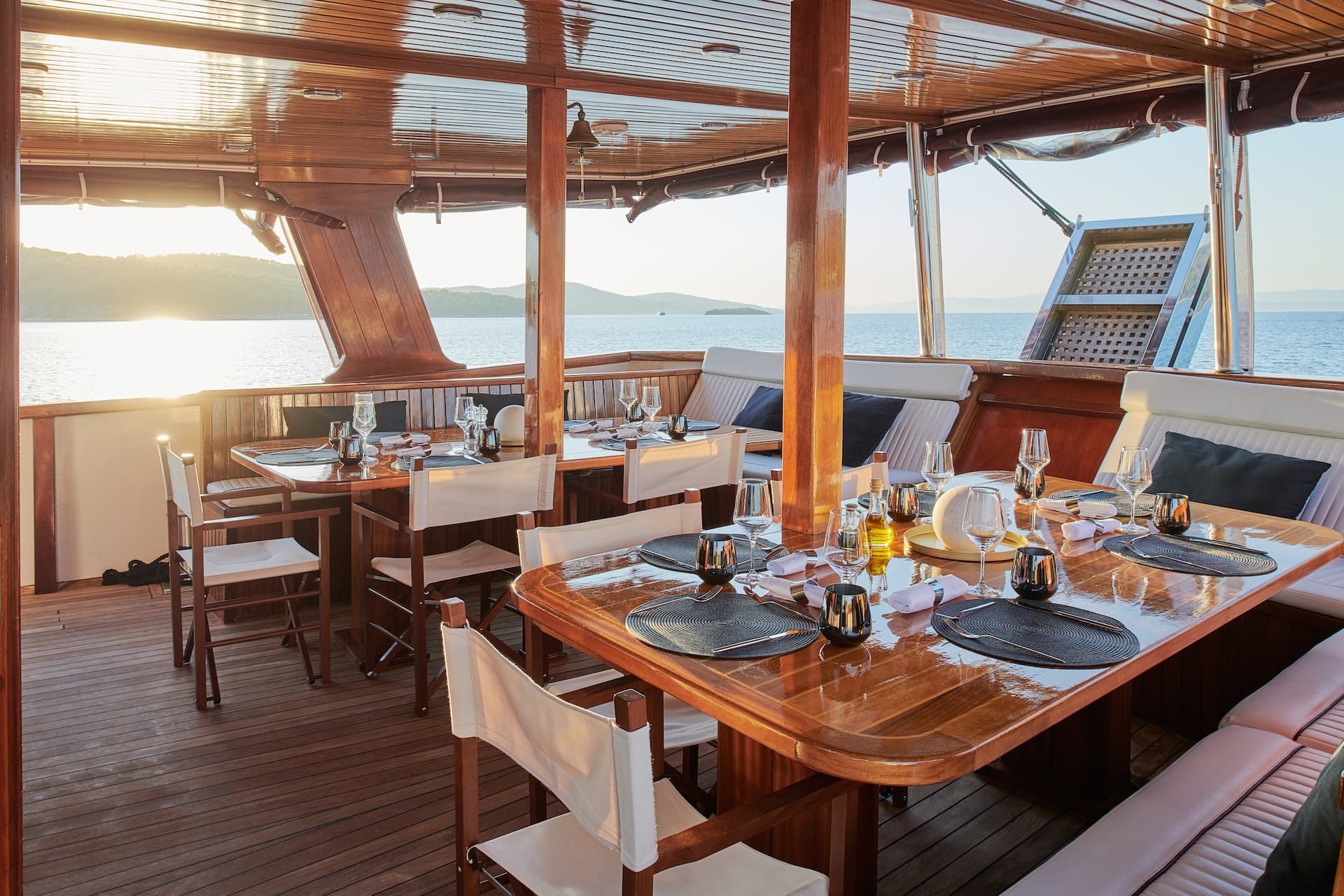 Outdoor dining area on a wooden yacht deck overlooking the sea at sunset