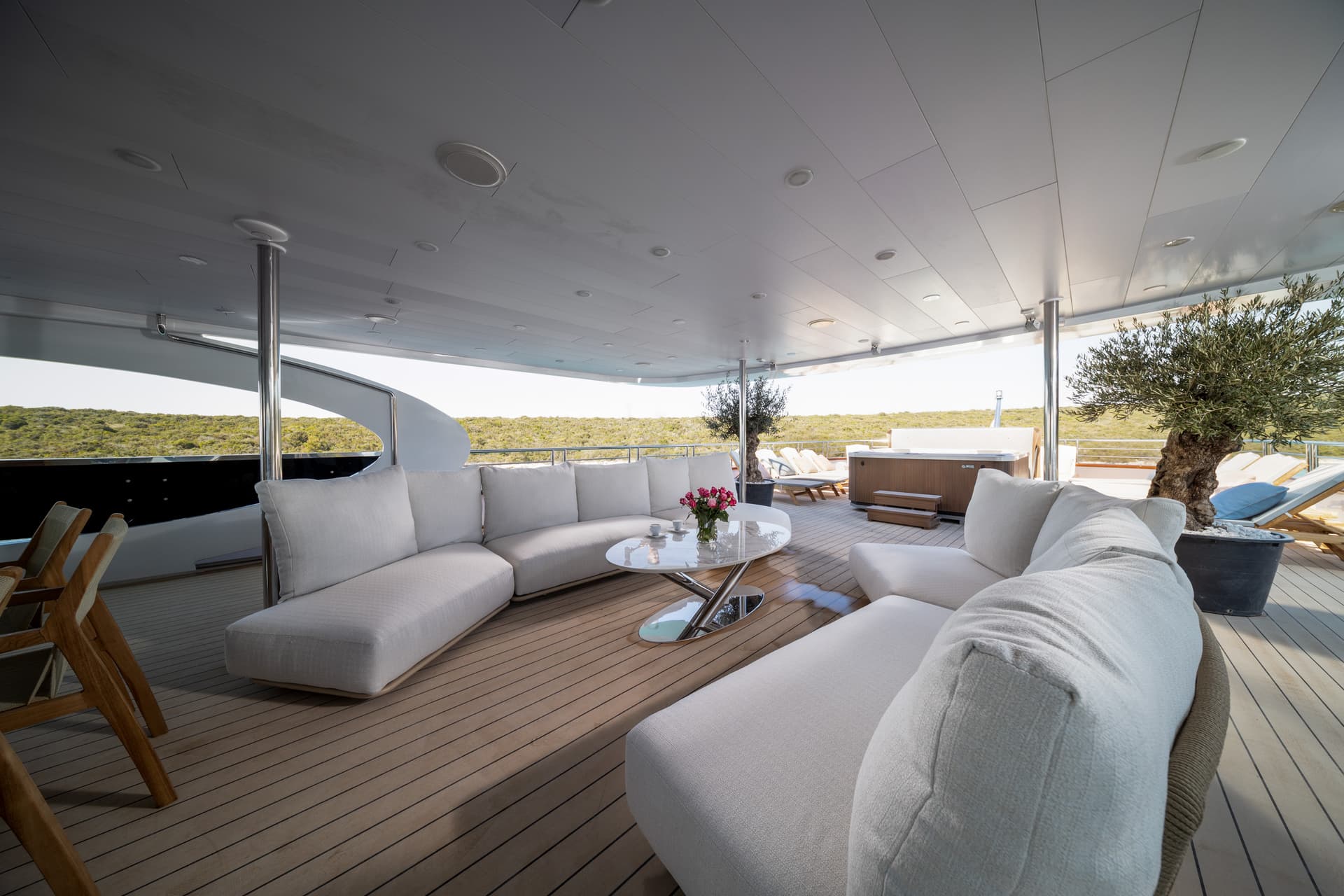 Luxury yacht exterior deck lounge with white seating, hot tub, and green coastline view.