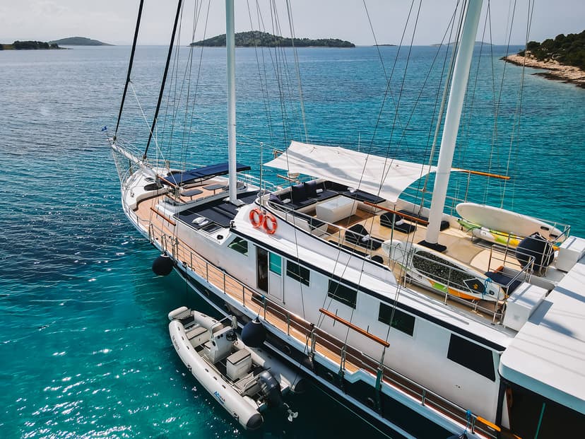 Large white yacht anchored in turquoise coastal waters near forested islands