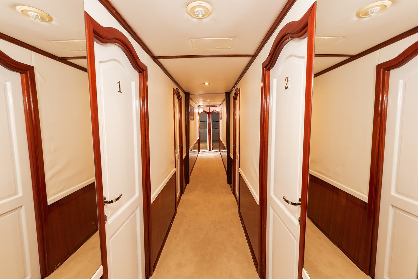 Narrow interior hallway with white doors numbered 1 and 2, wood trim, and beige carpet.