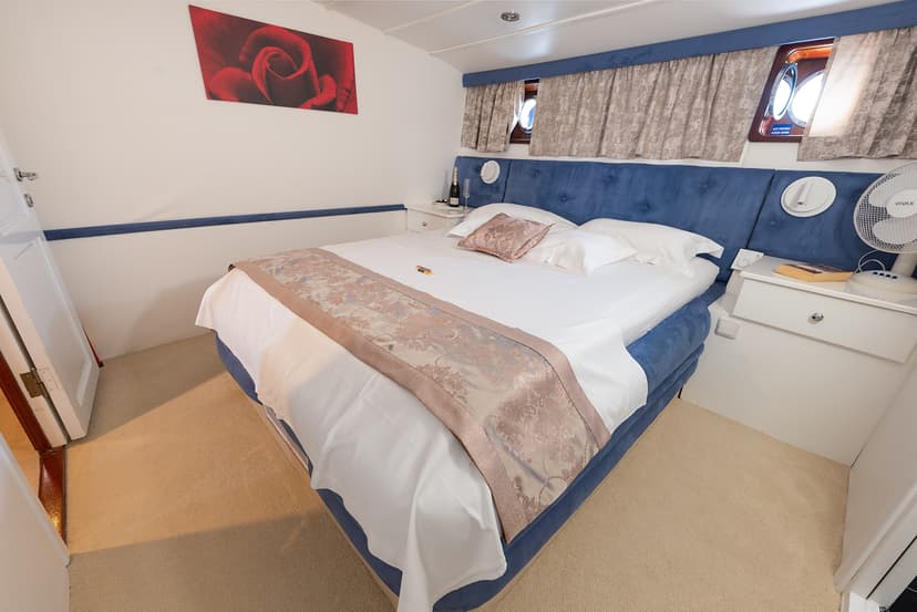 Cabin bedroom with blue velvet headboard, white linens, and porthole windows suggesting a boat setting.