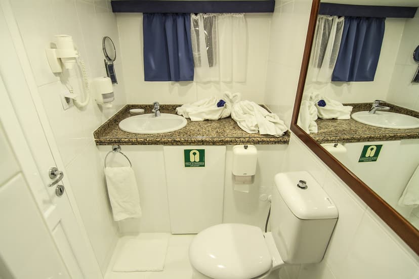 Small white bathroom with sink, toilet, mirror, and towels folded into swans.