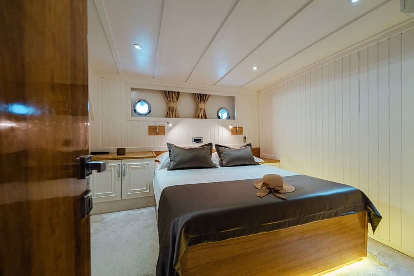 Comfortable double cabin bedroom on a Gulet with porthole windows and straw hat.