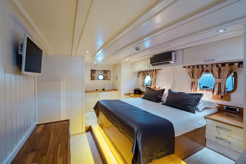 Master cabin interior on a gulet with white paneling, wood accents, and porthole windows.