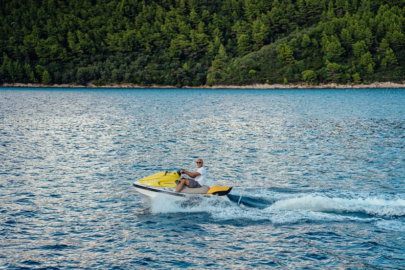 Man riding yellow jet ski on blue water near forested coastline