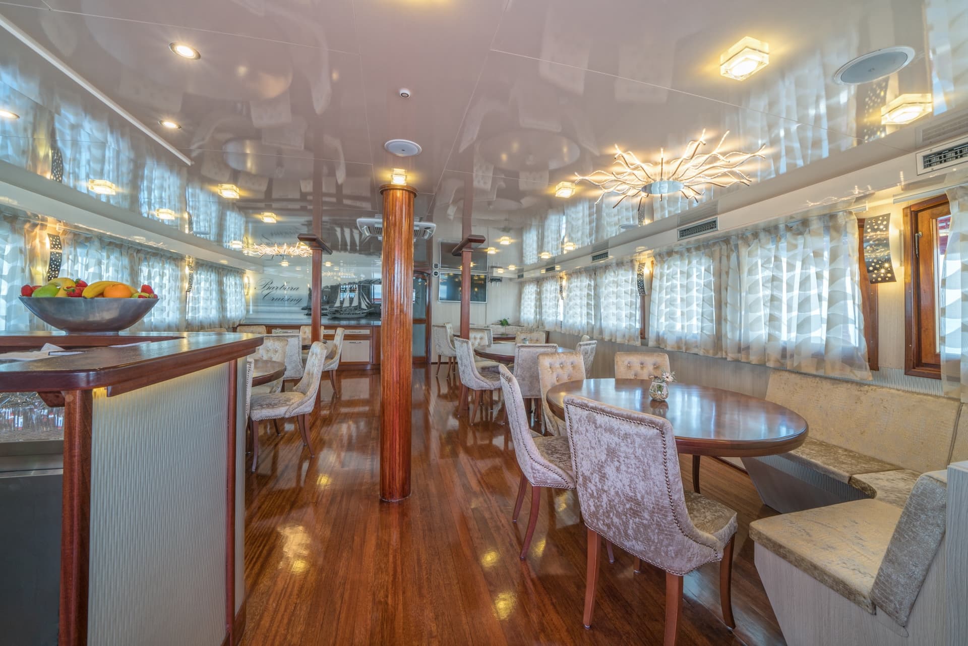 Interior dining lounge with polished wood floors, plush chairs, and a fruit bowl on the bar.