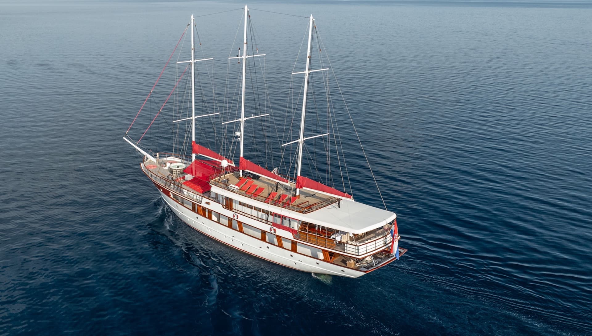 Three-masted gulet boat with red accents sailing on deep blue coastal waters