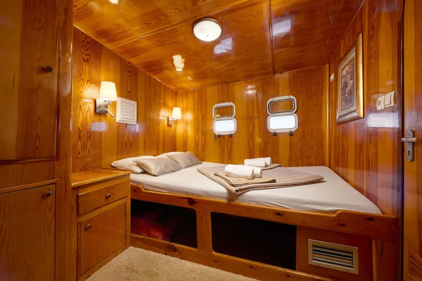 Cabin bedroom with wood paneling, bunk-style bed, and two oval porthole windows.