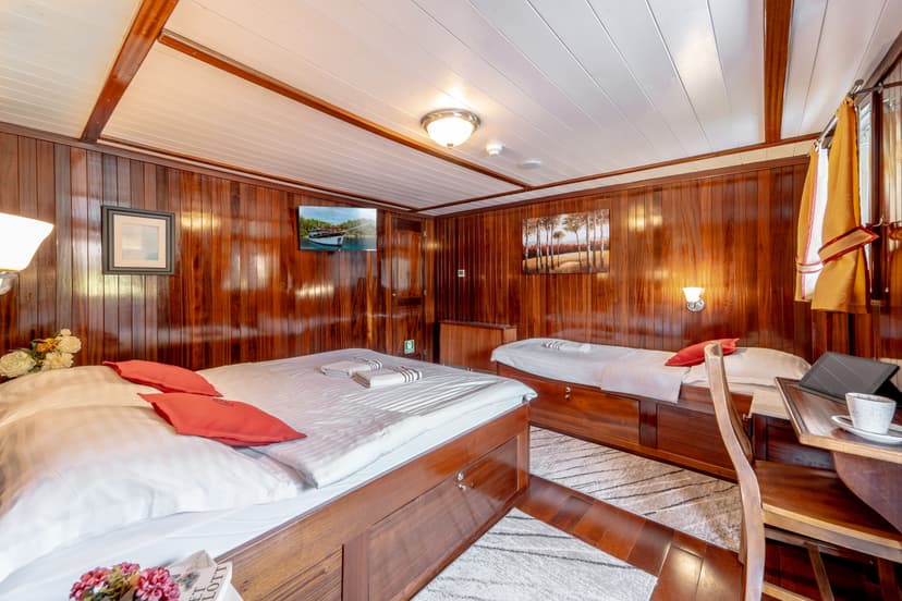 Cabin interior with polished wood paneling, white ceiling, and two beds with white linens.