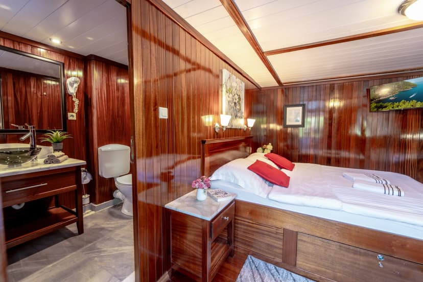 Cabin bedroom with glossy wood paneling, white ceiling, and adjacent small bathroom area.