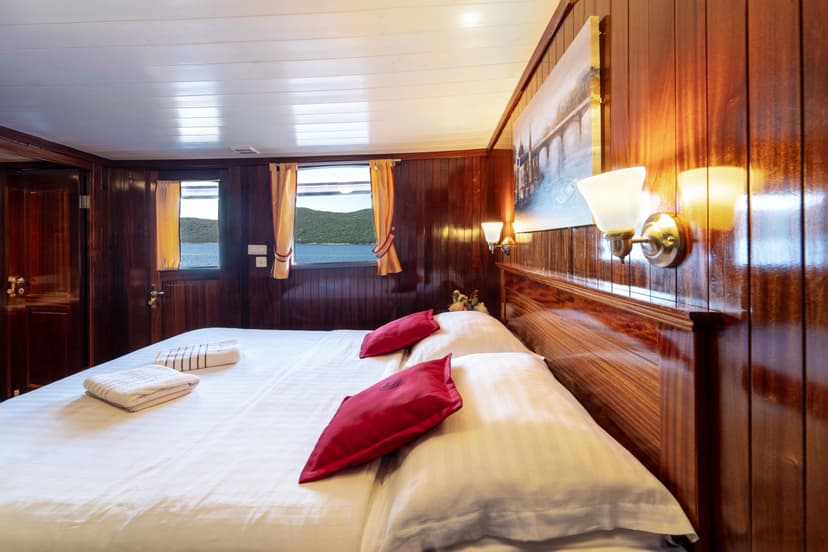 Cabin bedroom with white linens and wood paneling, view of sea and green island.