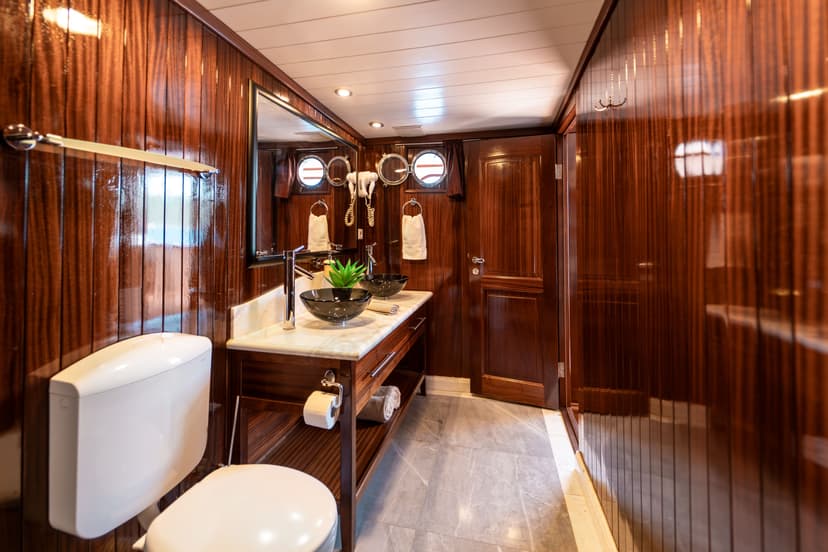 Bathroom interior with glossy wood paneling, marble vanity, dual black vessel sinks, and porthole windows suggesting a boat.