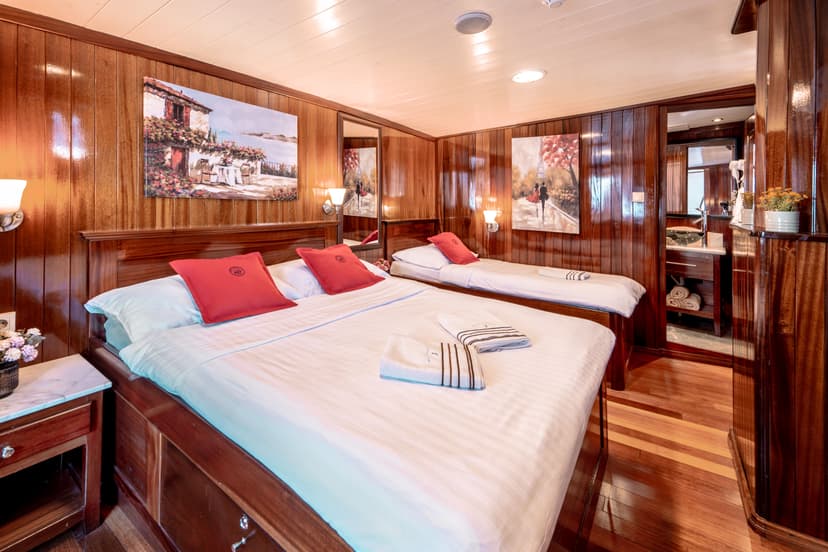 Cabin interior with glossy wood paneling, two beds with red pillows, and an ensuite vanity area.