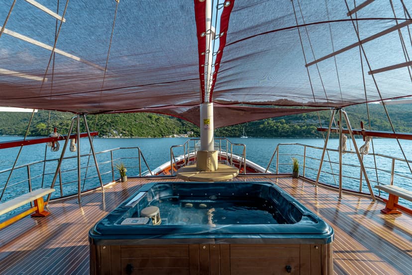 Jacuzzi on wooden boat deck with view of lush green coastline and blue sea