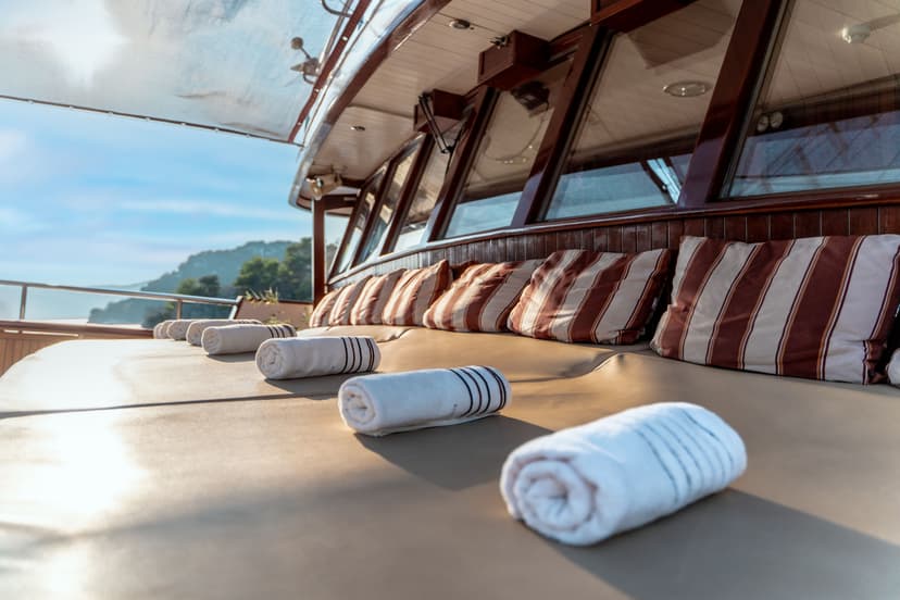 Sun deck on boat with rolled towels, striped pillows, and coastal hills in background