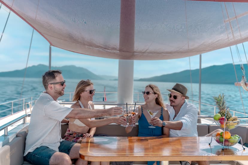 Four people toasting cocktails on a yacht deck with mountains in the background.