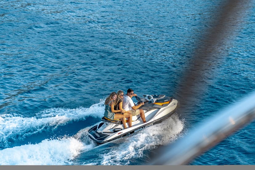 Three people riding a jet ski, creating white wake on deep blue water.