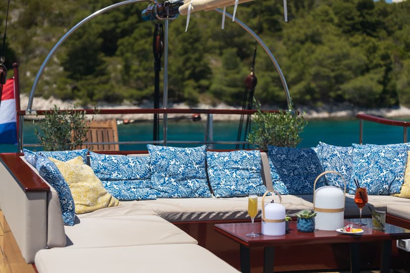 Boat deck lounge with blue patterned pillows overlooking turquoise water and green coastline