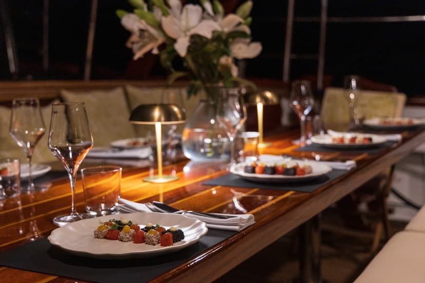 Fine dining appetizers and wine glasses on glossy wooden table, possibly on a yacht