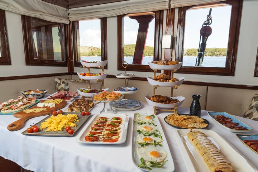 Breakfast buffet aboard a boat with views of a wooded coastline on the water.