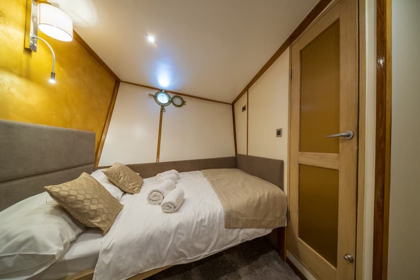 Cabin bedroom with double bed, porthole window, and wooden door on a boat.