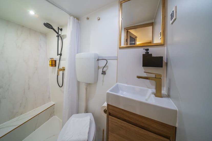 Small modern bathroom with white marble accents, gold fixtures, and wooden vanity cabinet.