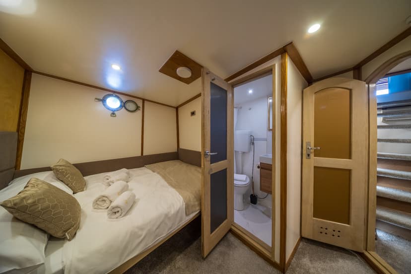 Cabin bedroom with double bed, porthole window, and ensuite bathroom entrance