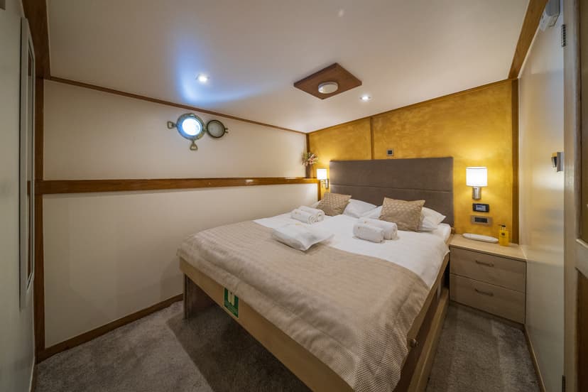 Cabin bedroom with double bed, porthole windows, and warm lighting on a ship.