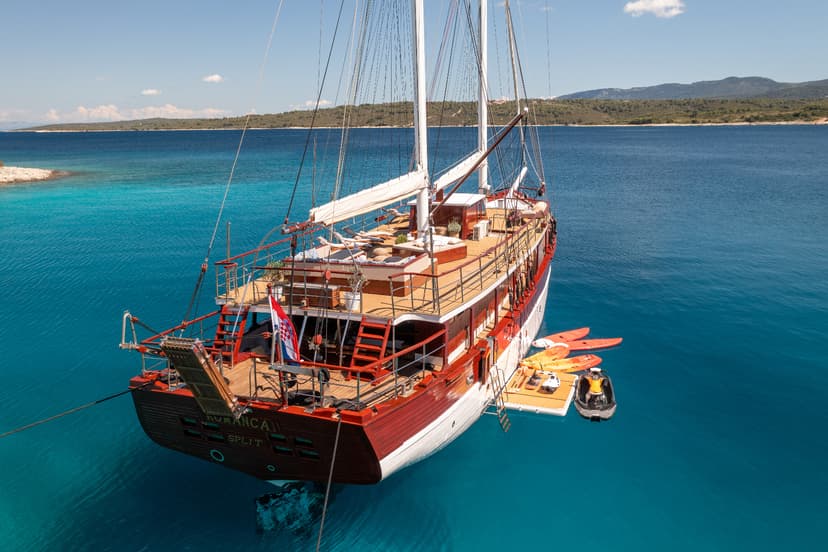 Large wooden sailboat named Romanca from Split anchored in turquoise coastal waters with islands in background.