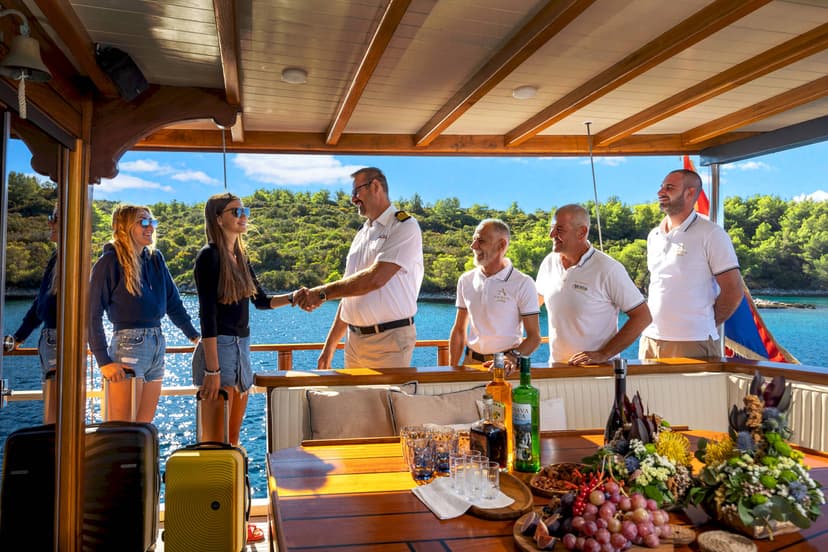 Crew greeting passengers with luggage aboard a boat near a lush, green coastline.