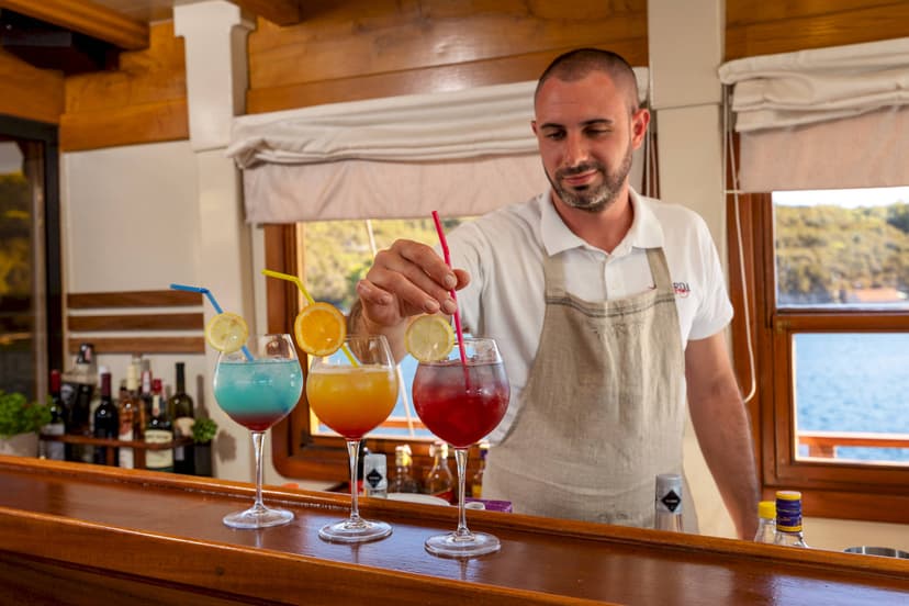 Bartender preparing colorful cocktails on a wooden bar with sea view from a boat.