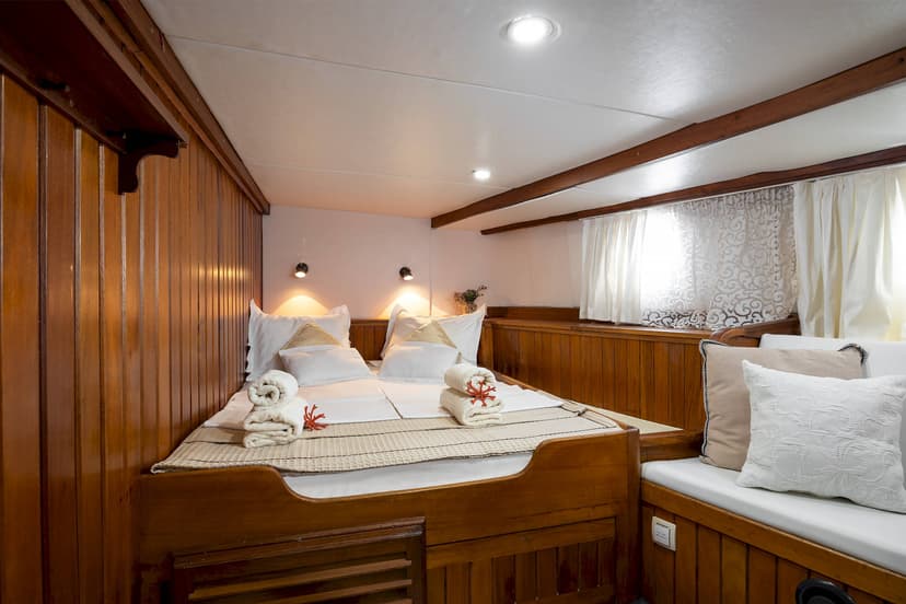 Cabin bedroom with wooden paneling, white bedding, and window with sheer curtains