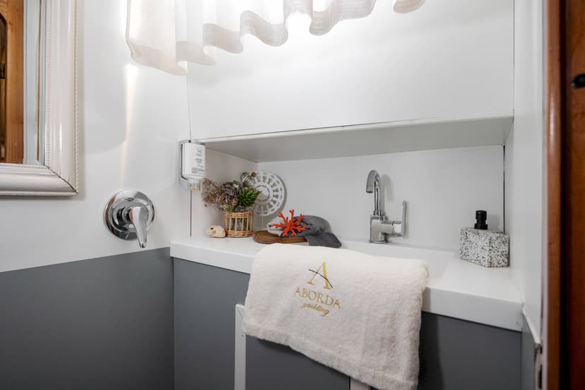 Bathroom vanity with sink, chrome fixtures, and white towel embroidered with ABORDA yachting logo.