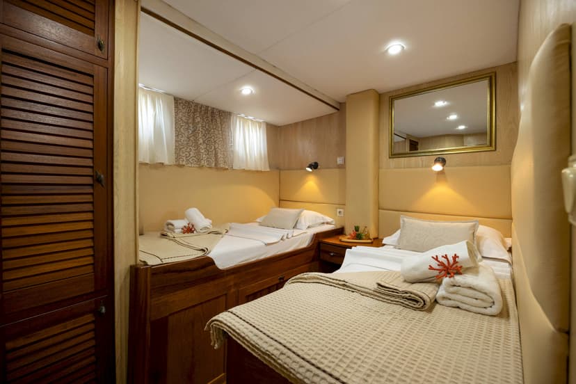 Twin cabin interior with wooden cabinetry, beige bedding, and a framed mirror on the wall.