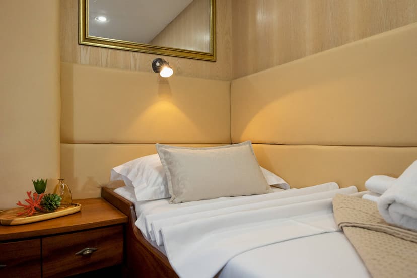 Cozy cabin or boat cabin bed with white linens, wooden nightstand, and reading light.