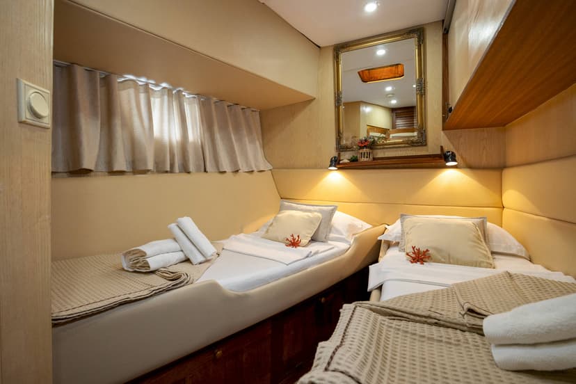 Twin cabin interior on a boat with beige padded walls, white linens, and a gold mirror.