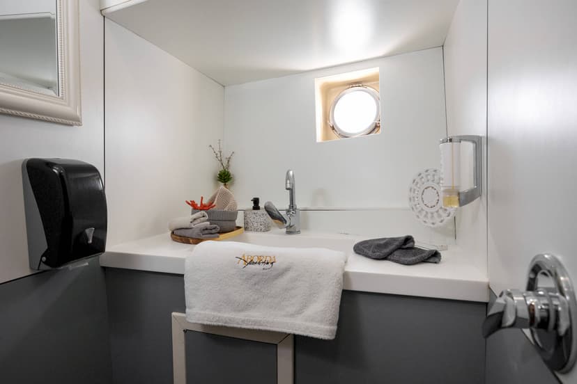 Small white bathroom with sink, porthole window, and ABORDA Yachting towel.