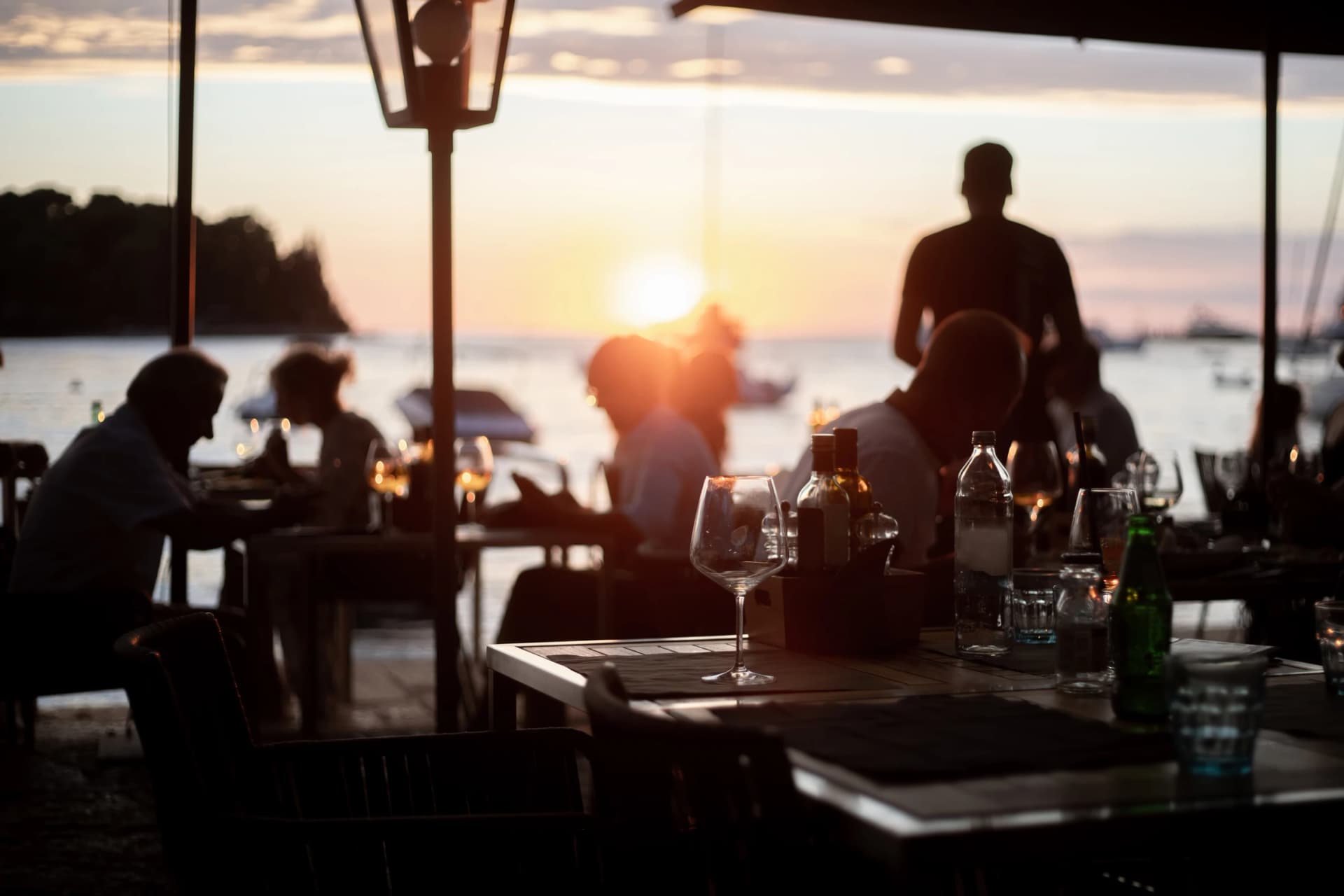people dining at seaside restaurant with romantic sunset