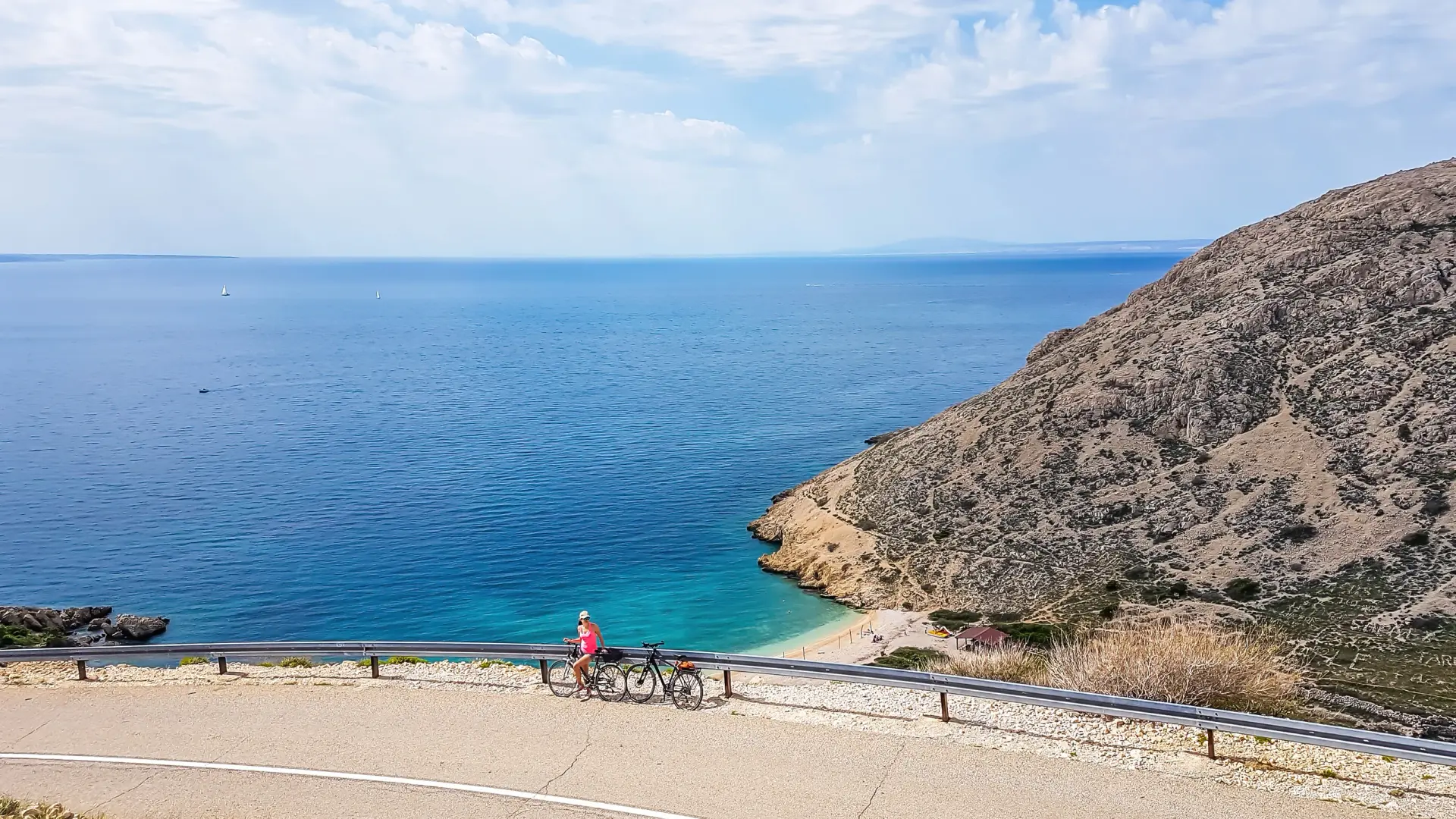 A girl in a sporty outfit, standing on the bike, on the side of a steep road. In the bottom Mediterranean Sea. Girl is enjoying the view. Thick clouds above. Active holidays. Hidden gem of Croatia