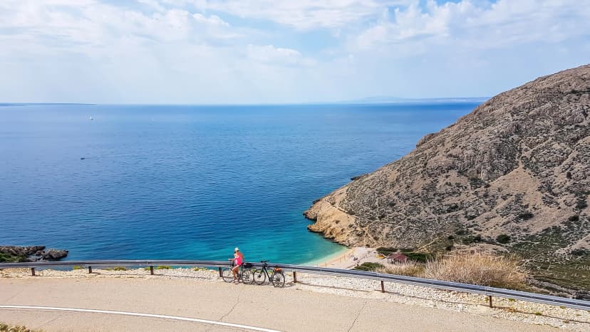 A girl in a sporty outfit, standing on the bike, on the side of a steep road. In the bottom Mediterranean Sea. Girl is enjoying the view. Thick clouds above. Active holidays. Hidden gem of Croatia