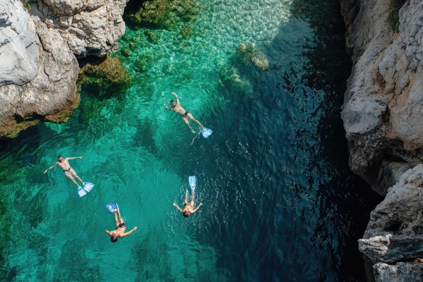 Tourists snorkeling in crystal clear water between cliffs in aerial view