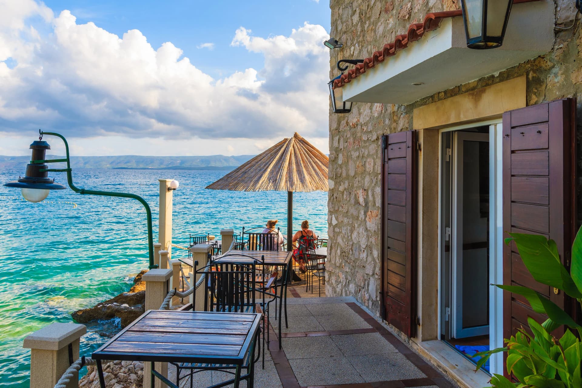 BOL PORT, BRAC ISLAND - SEP 8, 2017: Fishing restaurant tables and couple of people having drinks in Bol port at sunset time, Brac island, Croatia.