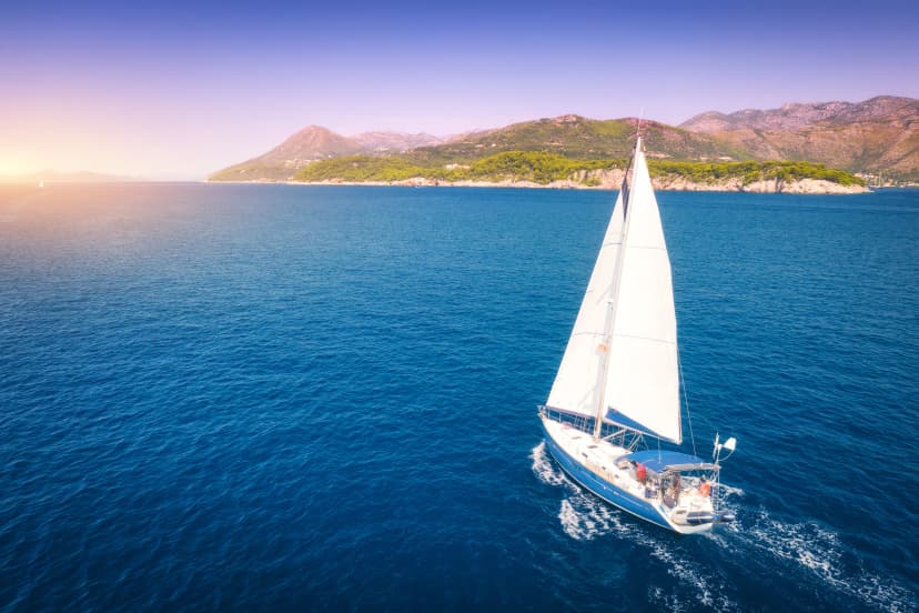 Aerial view of beautiful white sailboat in blue sea at bright sunny summer evening. Adriatic sea in Croatia. Landscape with yacht, mountains, transparent blue water, sky at sunset. Top view of boat
