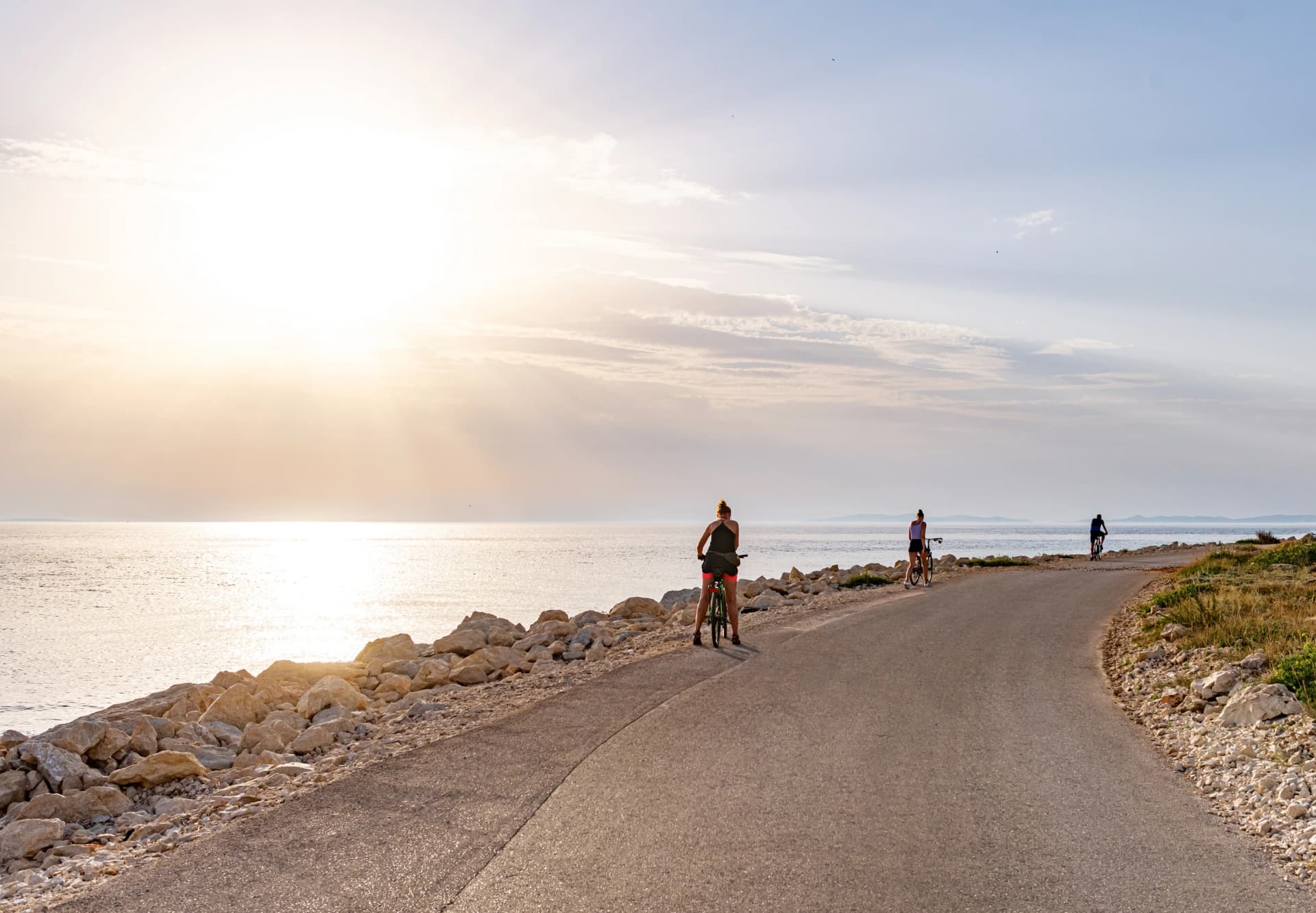 Cyclists on a country road by the sea in the rays of the sunset.